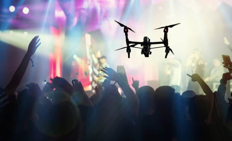Closeup silhouette of Drone flying for taking video of Concert crowd and Music fanclub with show hand action which follow up the songer at the front of stage, musical and concert concept