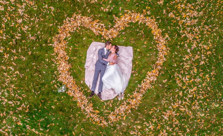 Aerial view of marriage couple lying in a shape of heart made of fall Autumn leafes woods drone photo romantic love .