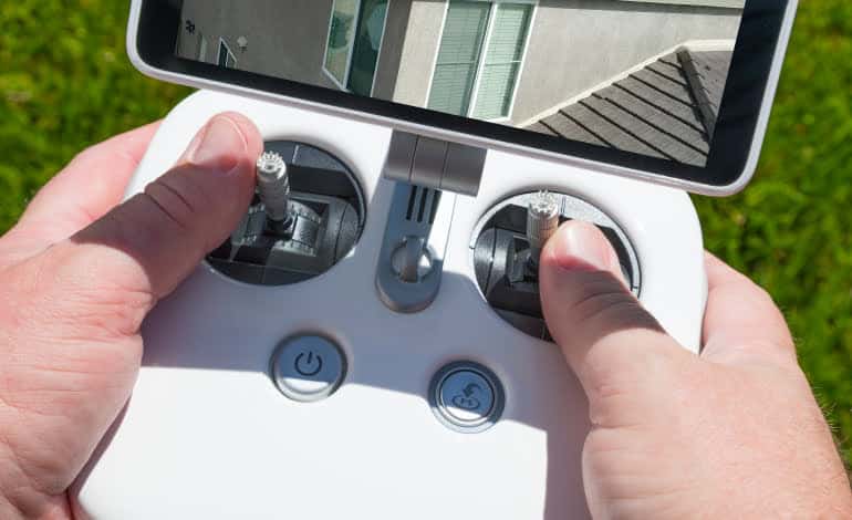 Hands Holding Drone Quadcopter Controller With Residential Roof Image on Screen.